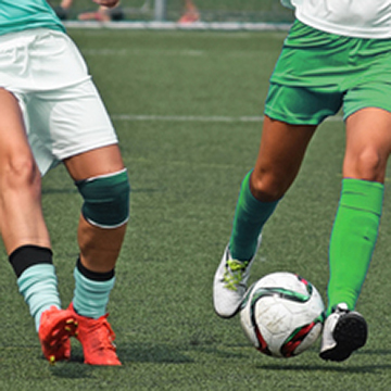 Two ladies racing after soccer ball.